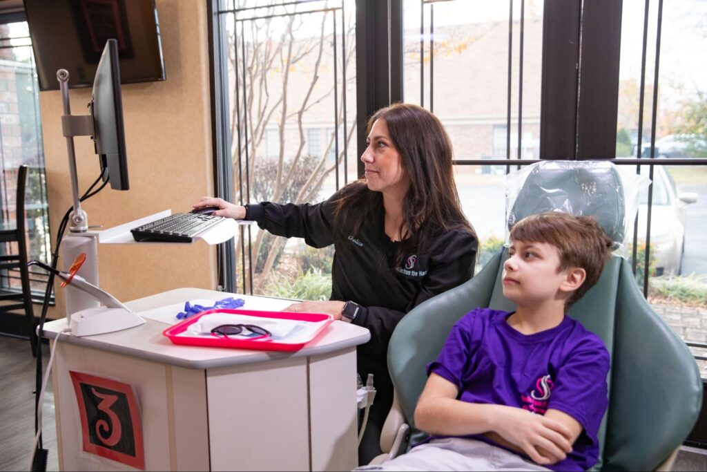 Orthodontist assisting child patient during digital assessment in a modern clinic, monitoring Invisalign treatment progress.
