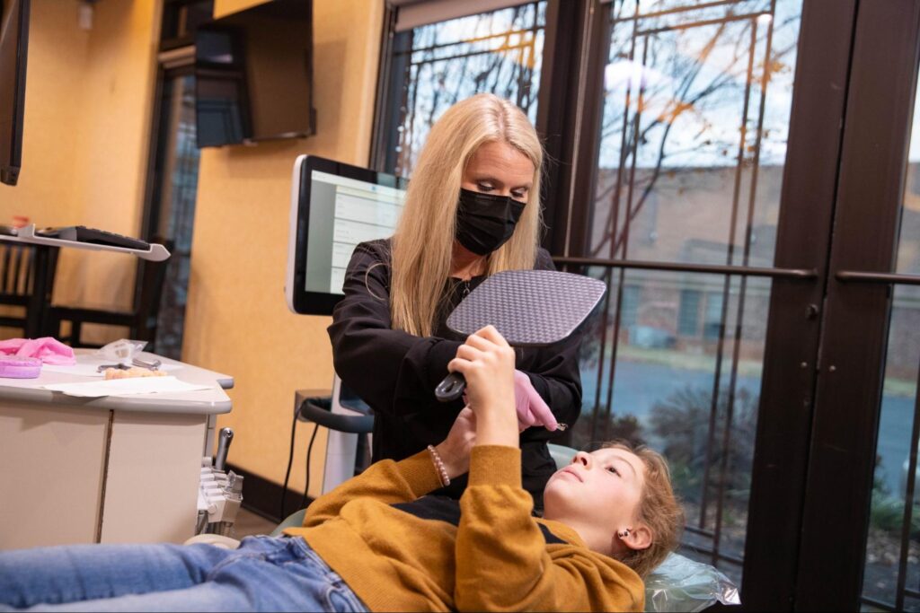 Dental professional assisting a patient with clear aligner fitting in an orthodontic office setting.