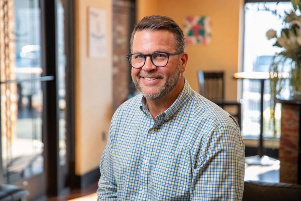Smiling man in glasses and checkered shirt seated in an orthodontic office, representing professional care at Smiles from the Hart Orthodontics.